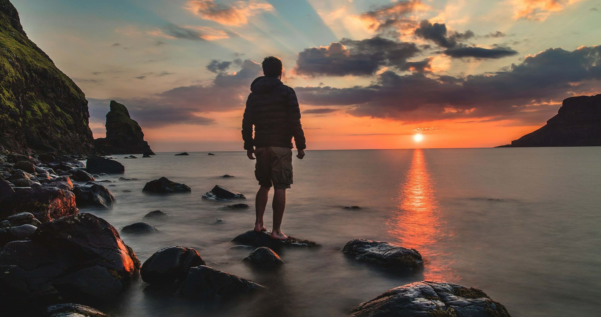 Man standing on stone looking at sunset.